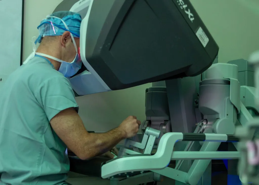 A surgeon seated at the console of a da Vinci Xi surgical robot, operating its controls.