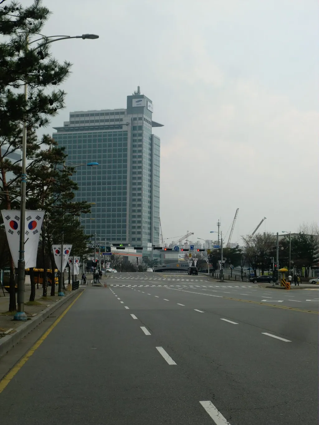 Samsung Electronics headquarters tower in Suwon, South Korea, viewed from a wide road lined with Korean flags.