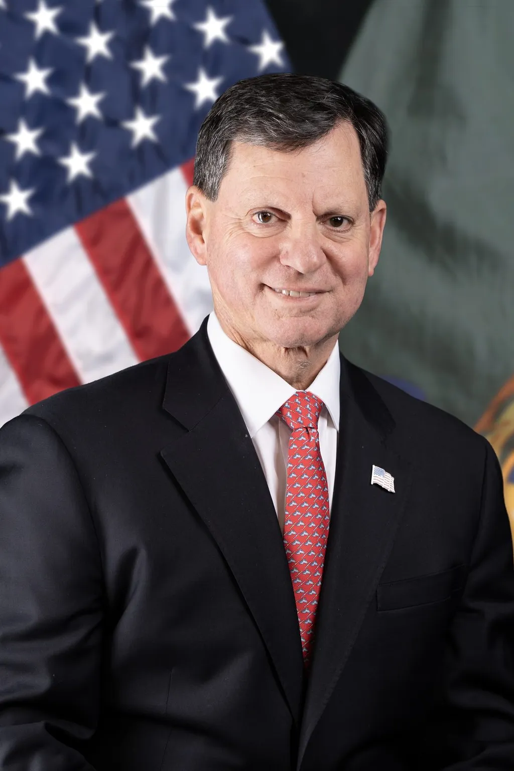 Official 2026 portrait of Frank J. Bisignano, the 18th Commissioner of the U.S. Social Security Administration, wearing a dark suit and red tie with a U.S. flag pin against a U.S. flag backdrop