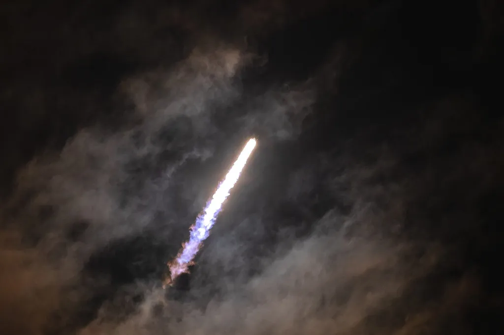 A SpaceX Falcon 9 rocket climbing through night clouds over Cape Canaveral, Florida, trailing a bright exhaust plume