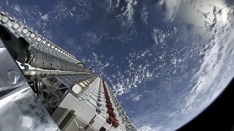 A stack of 60 Starlink satellites atop a Falcon 9 rocket shortly after launch, seen against Earth's curved horizon.