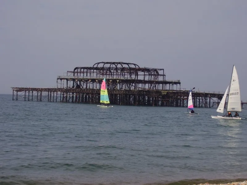 The ruined iron skeleton of Brighton's West Pier standing in the sea, with sailing boats in the foreground