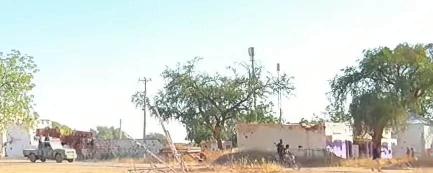 Rapid Support Forces fighters with an armed pickup truck on a street in el-Fasher, Sudan, 2025, with damaged buildings and a telecom mast visible. Real photograph of the story's subject (RSF in el-Fasher).