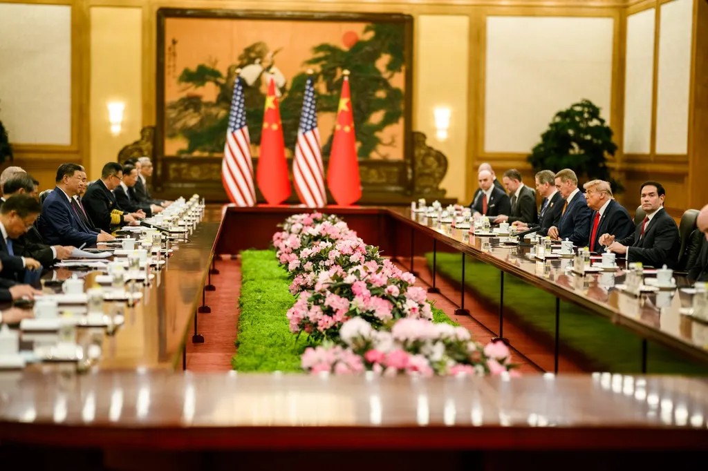 US President Donald Trump and Chinese President Xi Jinping seated across the table at a bilateral meeting in the Great Hall of the People, Beijing, with US and Chinese flags behind them.
