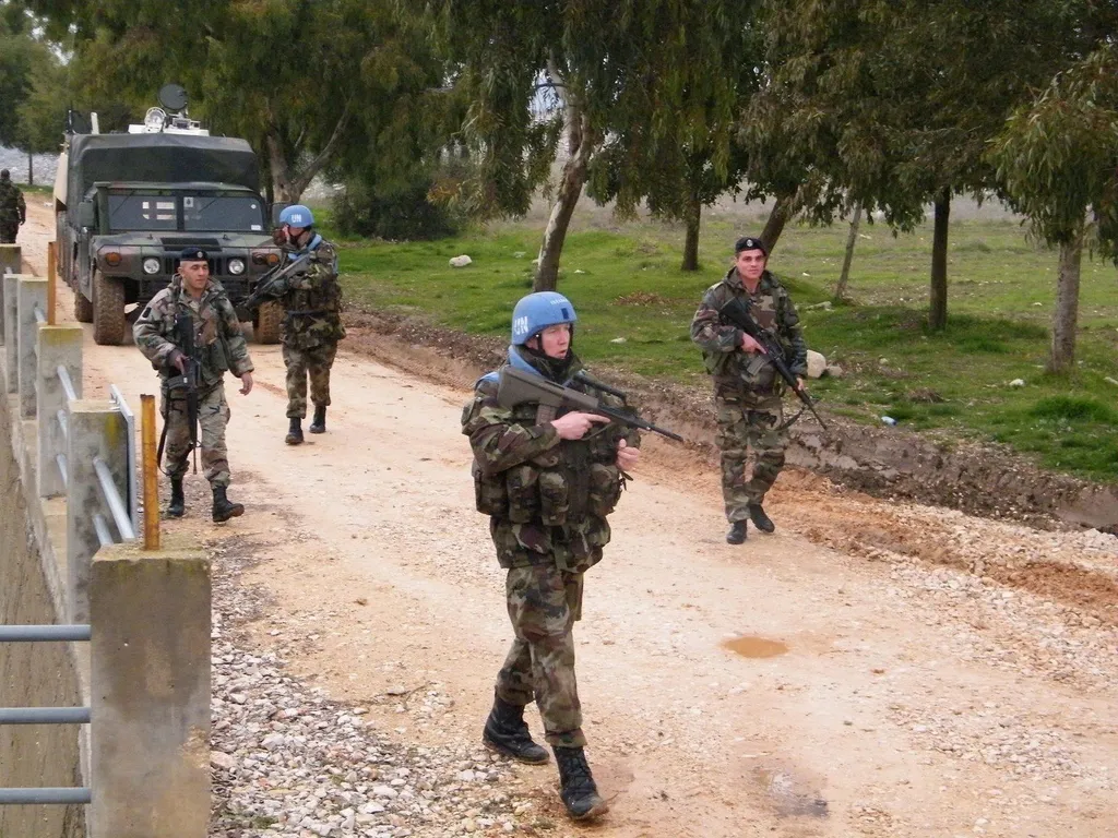 UNIFIL peacekeepers wearing UN-marked blue helmets on a foot patrol along a dirt road in southern Lebanon, with a military vehicle behind them.