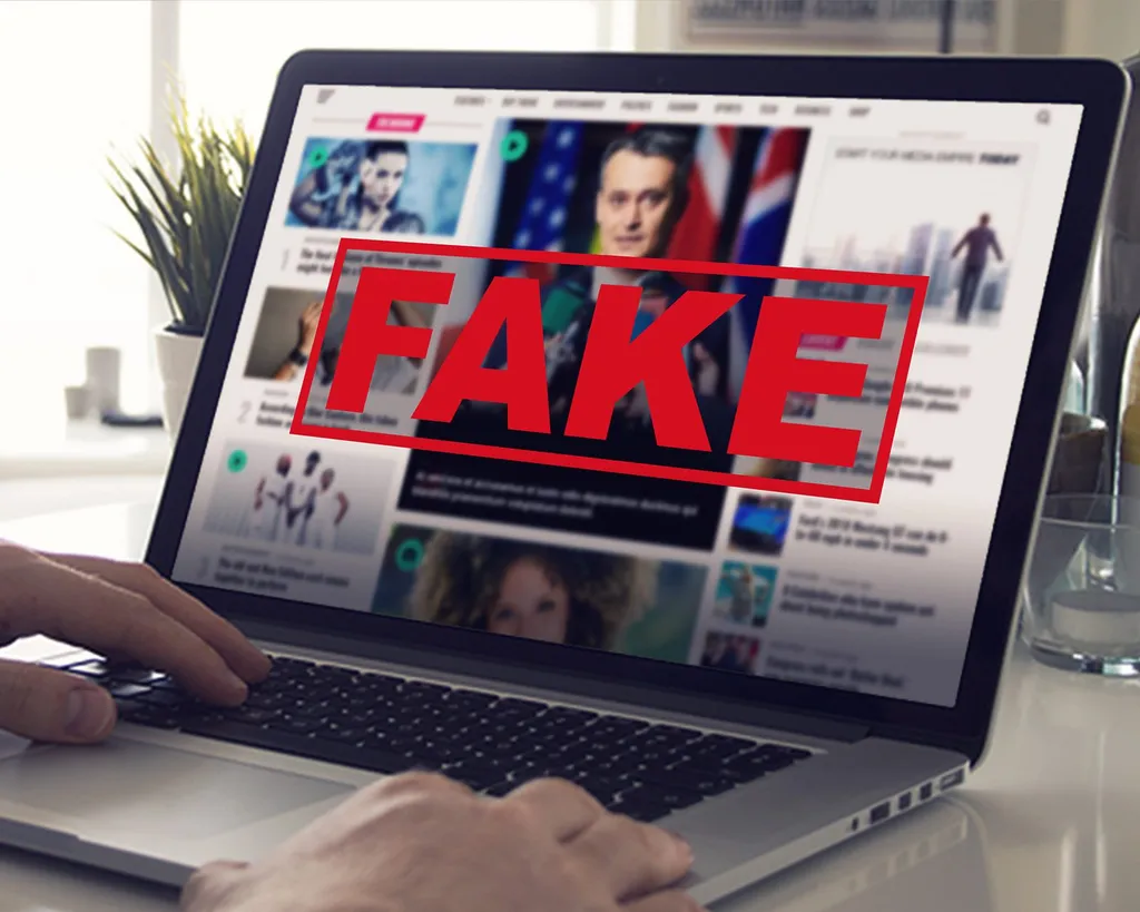 Illustration: a laptop displaying a news website stamped with a large red FAKE label, symbolising online disinformation. Illustration
