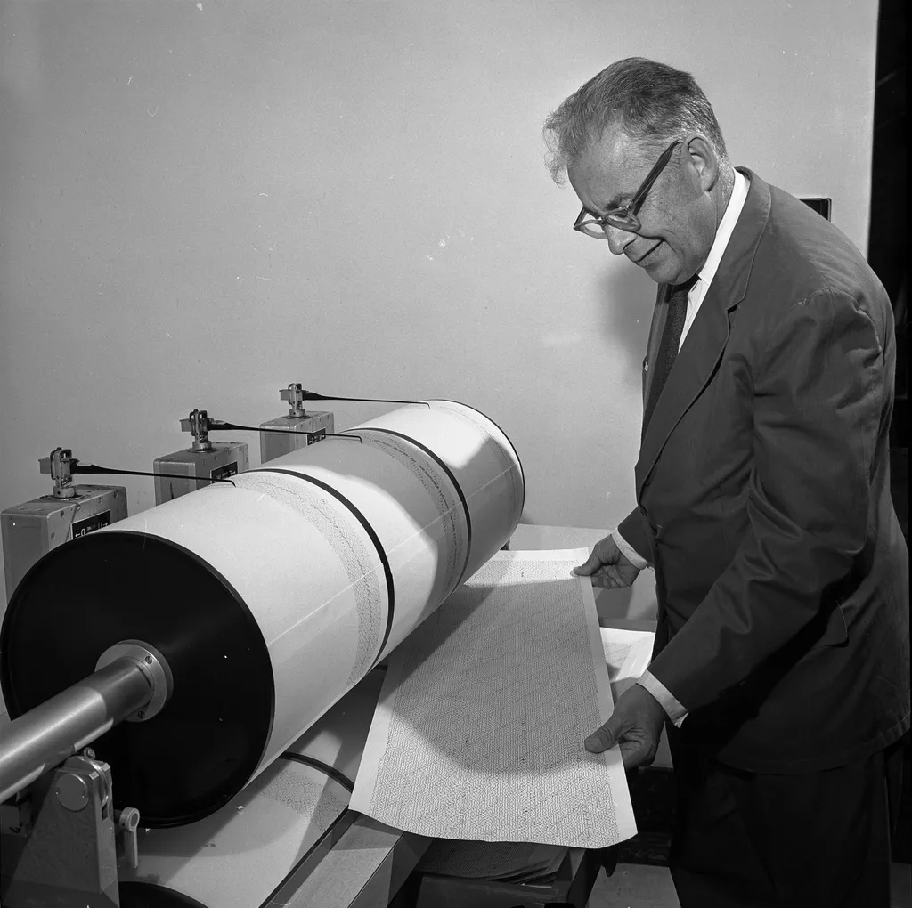 A man examining a seismograph recording drum with its paper trace