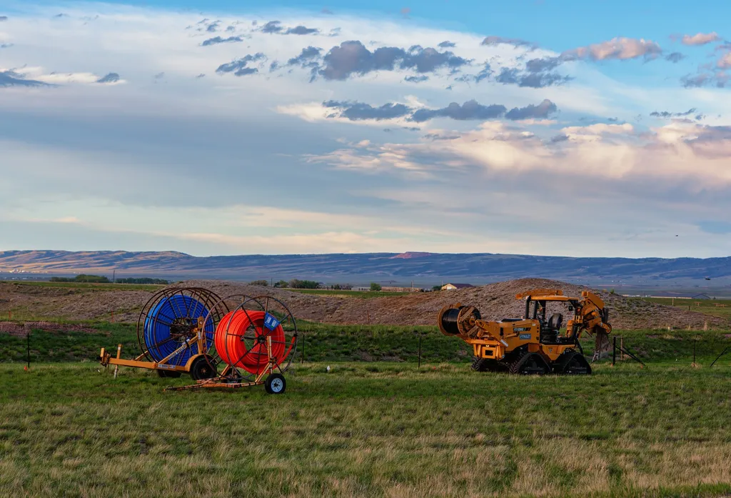 Fibre broadband installation equipment — cable reels and a cable plough — in a rural field in Laramie, Wyoming.