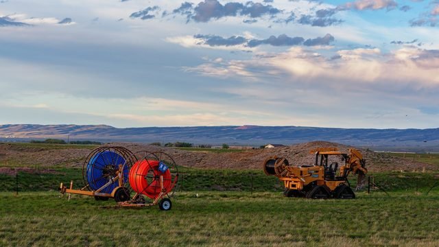 Fibre broadband installation equipment — cable reels and a cable plough — in a rural field in Laramie, Wyoming.